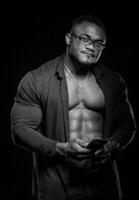noir et blanc portrait de le africain américain bodybuilder homme avec torse nu musclé torse. Masculin portant jeans isolé sur noir Contexte photo