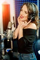 photo tournage dans le enregistrement studio. magnifique femme dans écouteurs. fille sur une studio Contexte souriant. mains près le écouteurs. portrait de une chanteuse.