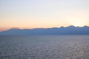 scénique vue majestueux Montagne intervalle à le coucher du soleil reflétant sur calme mer des eaux photo