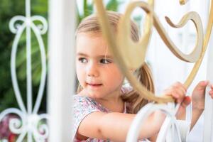 Jeune fille avec blond cheveux souriant derrière une charmant blanc piquet clôture photo