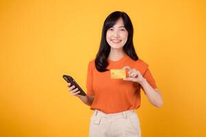 vif asiatique femme dans sa 30s, utilisant téléphone intelligent et mettant en valeur crédit carte sur vibrant Jaune Contexte. rapide en ligne achats Paiement processus. photo