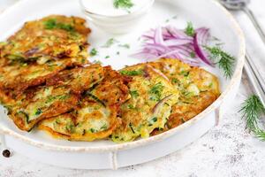 Zucchini beignets avec rouge oignons, Ail et herbes. végétarien Zucchini Crêpes et acide crème sur blanc tableau. photo