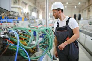 souriant et content employé. industriel ouvrier à l'intérieur dans usine. Jeune technicien avec difficile chapeau photo