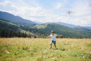 peu garçon fonctionnement sur une Contexte de montagnes avec cerf-volant. ensoleillé été journée. content enfance concept. photo