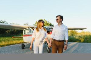 toute la longueur image de magnifique Jeune élégant couple près privé avion. en marchant sur piste dans aéroport dans de face de avion. photo