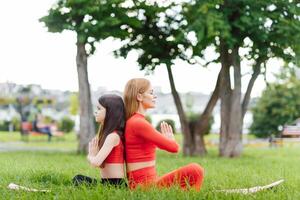 mère et fille Faire yoga des exercices sur herbe dans le parc à le journée temps. gens ayant amusement en plein air. concept de amical famille et de été vacances. photo