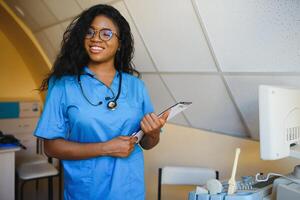 Jeune Afro-américain femelle médecin dans blanc manteau en utilisant ultra ultrason balayage machine et à la recherche sur le filtrer. africain femme médecin travail sur moderne ultrason équipement. photo