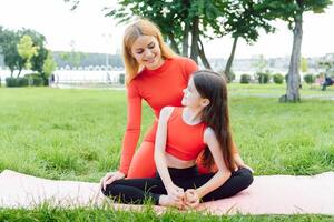 mère et fille Faire yoga des exercices sur herbe dans le parc à le journée temps. gens ayant amusement en plein air. concept de amical famille et de été vacances. photo