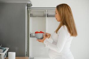 Enceinte femme à Accueil dans le cuisine ouvre le réfrigérateur photo