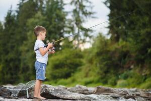 mignonne garçon dans blanc t chemise pêche dans le rivière et a amusant, sourit. vacances avec enfants, vacances, actif fins de semaine concept photo