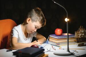 garçon apprendre cours dans le Accueil réglage à le table dans le lumière de une table lampe. photo