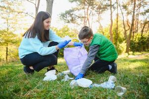 femme bénévole et peu garçon cueillette en haut le Plastique des ordures photo