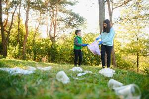 maman enseigne sa fils à nettoyer en haut poubelle dans la nature. une femme supprime Plastique bouteilles dans une sac. le sujet de environnement la pollution par ordures. photo