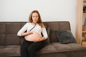 Enceinte femme en utilisant stéthoscope examiner sa ventre sur canapé, content Enceinte femme concept. photo