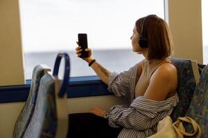 Jeune femme dans écouteurs fabrication photo sur téléphone tandis que en voyageant dans Publique transport