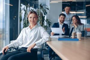 souriant sur de soi femelle patron séance sur réunion dans Bureau avec sa collègues à Contexte photo