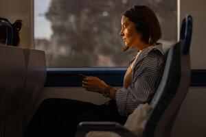 Jeune jolie femme Ecoutez la musique dans écouteurs et utilisation téléphone tandis que en voyageant dans Publique transport photo