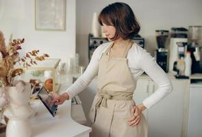 femelle barista dans tablier permanent à le compteur dans café magasin et prend ordres de client photo