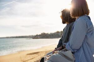 magnifique romantique couple séance à le plage portant décontractée vêtements et à la recherche à le océan photo