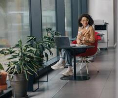 souriant affaires femme dans lunettes avoir une café Pause pendant travail sur portable dans confortable café photo