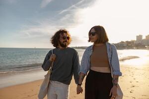 souriant romantique couple dans l'amour est marcher en portant mains à travers le plage sur le coucher du soleil photo
