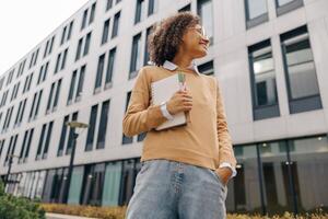 souriant femelle pigiste permanent avec Remarque tampons sur moderne bâtiment arrière-plans et regards une façon photo