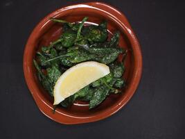 padron poivrons avec citron vert servi dans une plat isolé sur foncé Contexte Haut vue photo