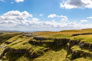 ensoleillé paysage de roulant collines avec rocheux falaises et vert herbe en dessous de une bleu ciel avec des nuages à Malham crique, Yorkshire, Royaume-Uni. photo