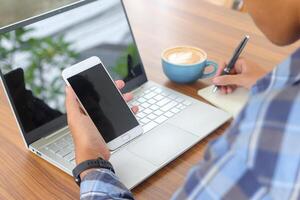 proche en haut de Masculin main l'écriture sur Remarque livre avec stylo, montrant Vide écran de portable et téléphone intelligent. travail dans café concept avec une tasse de café photo