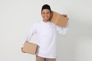 portrait de content excité asiatique musulman homme Aller Accueil pour eid moubarak. indonésien gars porter papier carton boîte. isolé image sur blanc Contexte photo
