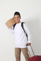 portrait de attrayant asiatique musulman homme porter papier carton boîte et valise et permanent avec confiant. Aller Accueil pour eid moubarak. isolé image sur blanc Contexte photo