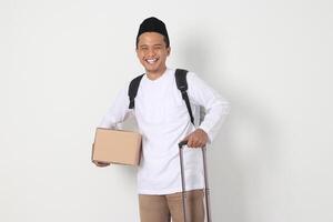 portrait de excité asiatique musulman homme dans koko chemise avec peci porter papier carton boîte et en portant valise gérer. Aller Accueil pour eid moubarak. isolé image sur blanc Contexte photo