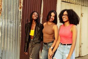 multiracial groupe de Trois copains en marchant vers le bas le ville rue. Trois Jeune femmes en marchant en plein air. photo