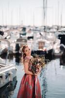 Jeune modèle fille dans une magnifique robe avec une bouquet de fleurs sur le plage dans France. fille avec fleurs dans printemps Provence sur le français riviera photo