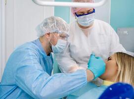 une dentiste portant une protecteur masque est assis proche et détient instruments dans le sien mains avant traiter une patient dans le dentaire Bureau photo