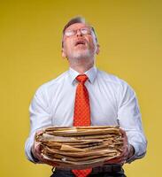 une homme d'affaire porter pile de formalités administratives. Jaune Contexte. triste expression. à faire une lot photo