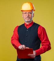 ingénieur dans une casque sur une Jaune Contexte. Sénior homme en portant presse-papiers. photo