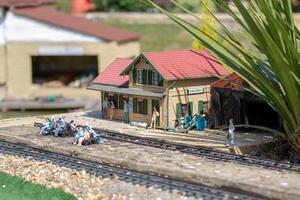miniature modèle de une train station avec minuscule Les figures et des pistes, entouré par réaliste aménagement paysager. photo