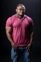 plein longueur vue de le africain américain bodybuilder permanent en toute confiance sur noir studio Contexte. homme démontrant le sien à la mode vêtements photo