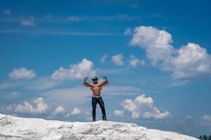 impressionnant athlétique Jeune gars avec nu torse. musclé Beau torse nu bodybuilder permanent sur une bleu ciel. photo
