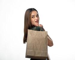 Jeune femelle est en portant épicerie achats sac. des stands sur blanc Contexte. femme à la recherche derrière dos. Jeune fille est en portant lumière marron achats sac derrière dos. isolé Contexte. fermer. photo