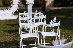 décor à le mariage. blanc chaises décoré avec blanc fleurs, sur vert herbe. photo