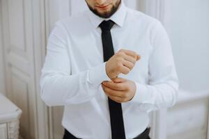 le homme mettre sur le sien chemise et se redresse boutons de manchette. le jeune marié boucler boutons de manchette sur le menottes de le chemise. le homme d'affaire boucler boutons de manchette sur le menottes de le chemise. concept réussi homme d'affaire. photo