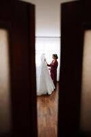 Matin portrait de une luxueux et magnifique la mariée dans une Hôtel dans une luxueux pièce dans rouge pyjamas permanent suivant à sa mariage robe. photo