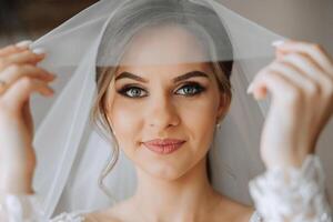 magnifique Jeune la mariée en portant voile dans blanc mariage robe, portrait de brunette la mariée dans Hôtel chambre, Matin avant mariage. photo