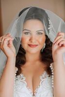 magnifique Jeune la mariée en portant voile dans blanc mariage robe, portrait de brunette la mariée dans Hôtel chambre, Matin avant mariage. photo