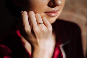 Matin de luxueux et magnifique la mariée dans Hôtel dans luxueux pièce dans rouge pyjamas avec or bague sur doigt fermer. photo