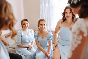 demoiselles d'honneur réjouir dans le matin, portion à boucler le boutons sur le mariage robe et préparer pour le mariage cérémonie. elles ou ils prendre des photos, sourire, Aidez-moi le la mariée avec sa chaussures. photo