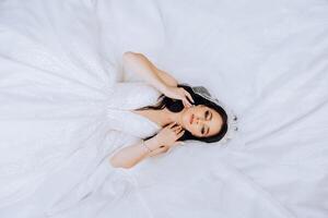 une brunette la mariée mensonges sur une dentelle robe, pose avec fermé yeux, émouvant sa cheveux. photo