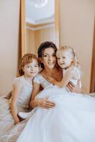 le la mariée est photographié avec petit les enfants sur le mariage journée. une peu fille baisers sa la mariée sur le joue. photo